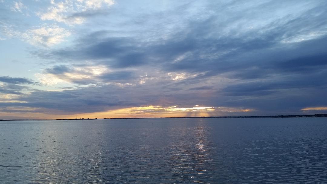 Photo of a sunrice over a body of water breaking through clouds.